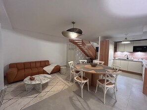 A modern living room with a brown sofa, a round coffee table, and a dining area with white chairs and a wooden table. - Villa Rosa By Avecoeur (Sainte-Maxime)
