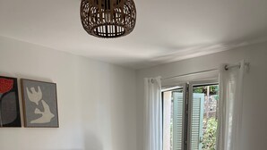 A bedroom with a bed, a nightstand, a lamp, a wall art piece, and a view through a window with shutters. - Villa Rosa By Avecoeur (Sainte-Maxime)