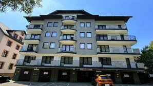 A multi-story building with balconies, a parking area, and a car parked in front. - Art Apartament Krynica Zdrój Centrum (Krynica-Zdrój)