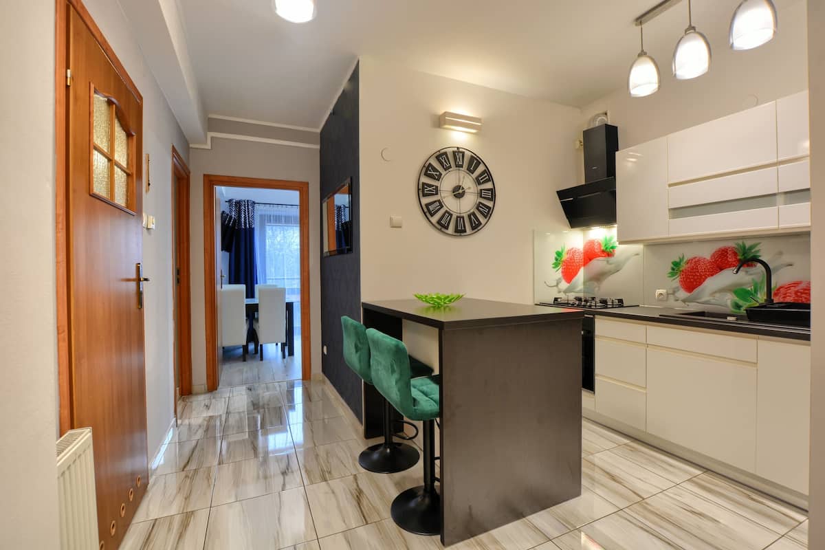 Una cucina moderna con isola centrale, orologio a parete e zona pranzo con una sedia.