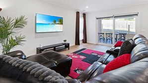 Ein modernes Wohnzimmer mit Flachbildfernseher, Ledersofa und Blick auf eine Terrasse.