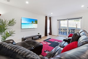 Ein modernes Wohnzimmer mit Flachbildfernseher, Ledersofa und Blick auf eine Terrasse.