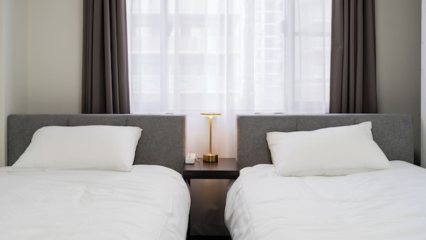 Ein Hotelzimmer mit zwei Betten, einem Nachttisch mit Lampe und einem Fenster mit Vorhängen.