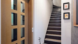 Ein Hotelkorridor mit einer Holztür, einer roten Fußmatte, einer Treppe und gerahmten Bildern an der Wand.