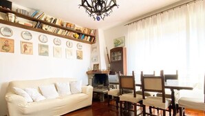 Ein Wohnzimmer mit Sofa, Holzboden, einer Kandelaber, einem Bücherregal und einem Essbereich mit Stühlen und Tisch.