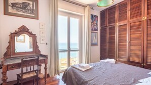 Ein Schlafzimmer mit einem Bett, einem Holztisch, einem Stuhl, einem großen Fenster mit Aussicht und einem Gemälde an der Wand.