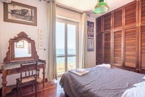 Ein Schlafzimmer mit einem Bett, einem Holztisch, einem Stuhl, einem großen Fenster mit Aussicht und einem Gemälde an der Wand.