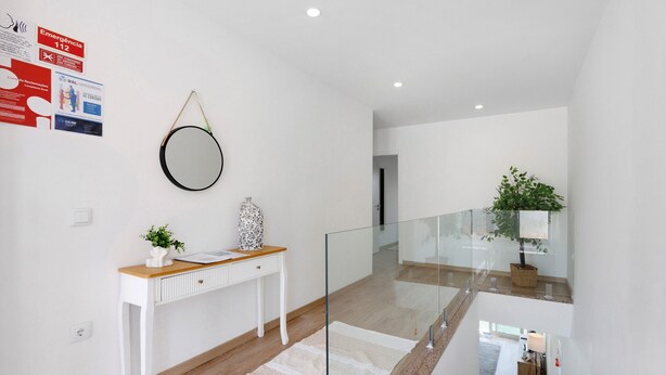 A modern interior with a white console table, a round mirror, and a glass railing. - ManuelHouse – Modern Two-Story Home in Vila Nova de Gaia (Vila Nova de Gaia)