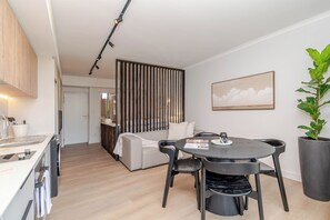 Une cuisine moderne dotée d’un four encastré, un coin repas avec une table ronde et des chaises, un canapé et une grande plante en pot.