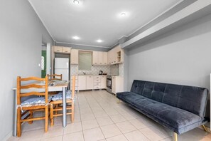 Un espace de vie compact comprenant un coin cuisine, un coin repas avec des chaises en bois et un canapé de couleur foncée.