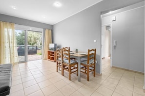 A modern living room with a dining area, a TV, and a sliding glass door leading to a balcony. - Abatis CityHome (Lefkada)