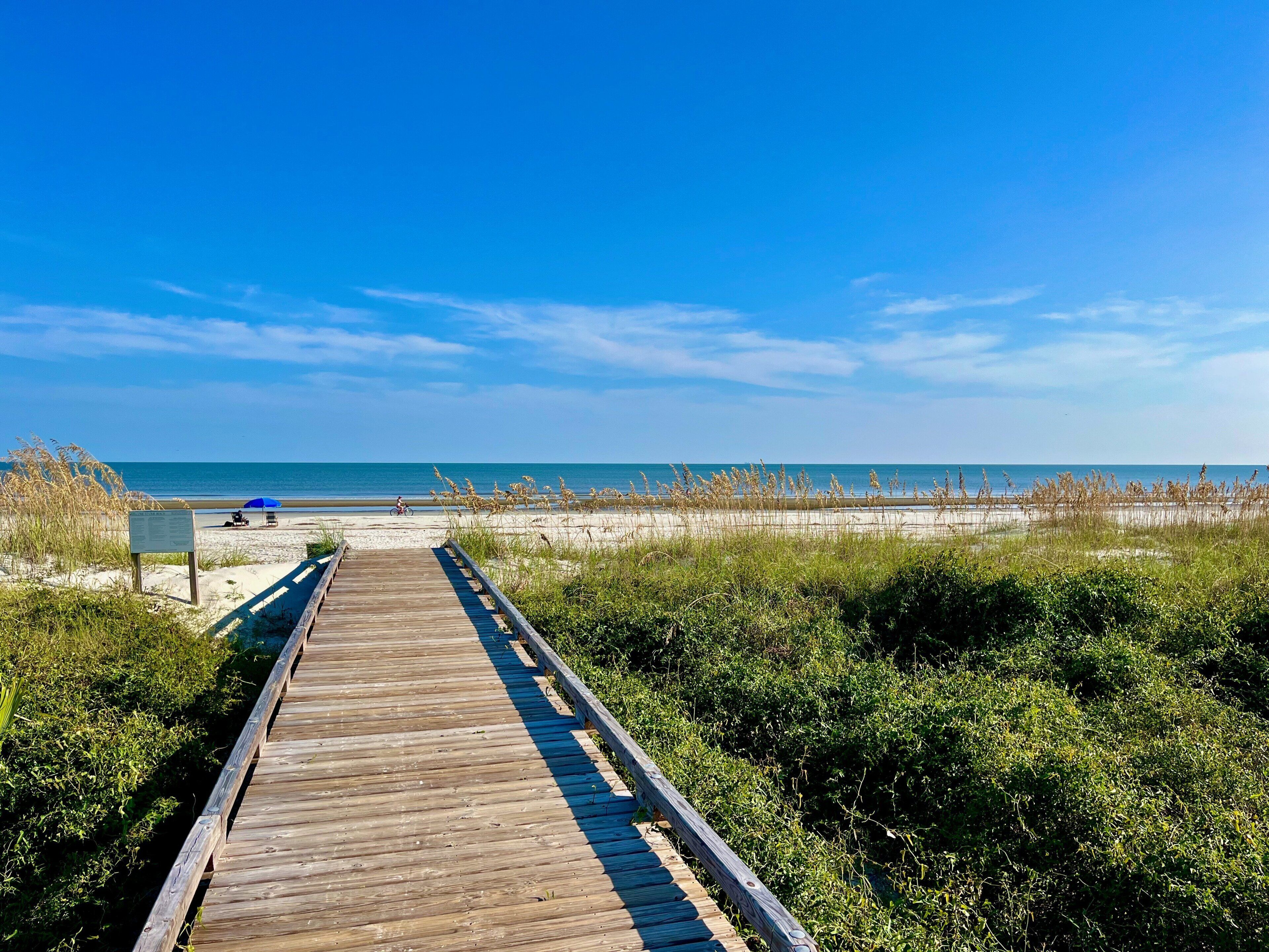 Une promenade en bois menant à une plage, avec un ciel bleu dégagé.