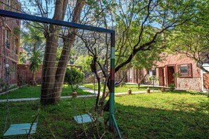 A courtyard with a swing set, trees, and a stone building. - Beautiful 7-bedroom hotel in tranquil Aghbalou perfect for groups (Ourika)