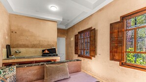 Quarto com cozinha compacta, um banco acolchoado, janela com detalhe decorativo e iluminação embutida no teto.