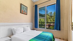Quarto com cama, mesa de cabeceira, janela com cortinas e um quadro na parede.