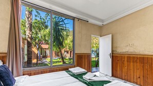 Quarto com uma grande porta de correr de vidro, cama com roupa de cama branca e tapete verde.
