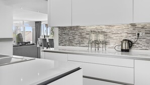 A modern kitchen with white cabinetry, a tiled backsplash, and a kettle on the counter. - Villa Elviria (Marbella)