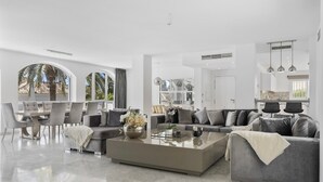 A spacious living area with a large coffee table, grey sofas, and a dining area with chairs. - Villa Elviria (Marbella)