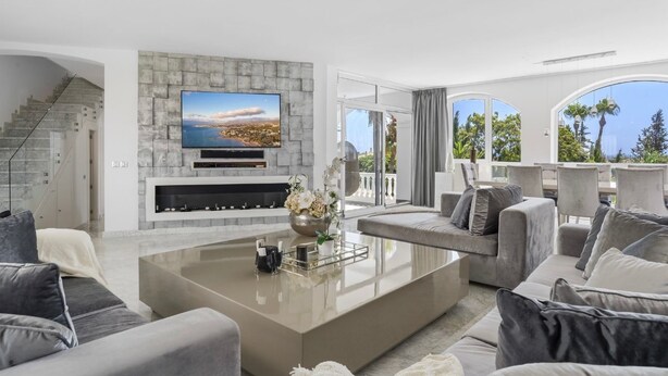 A modern living room with a stone fireplace, a flat-screen TV, and a balcony with a view. - Villa Elviria (Marbella)