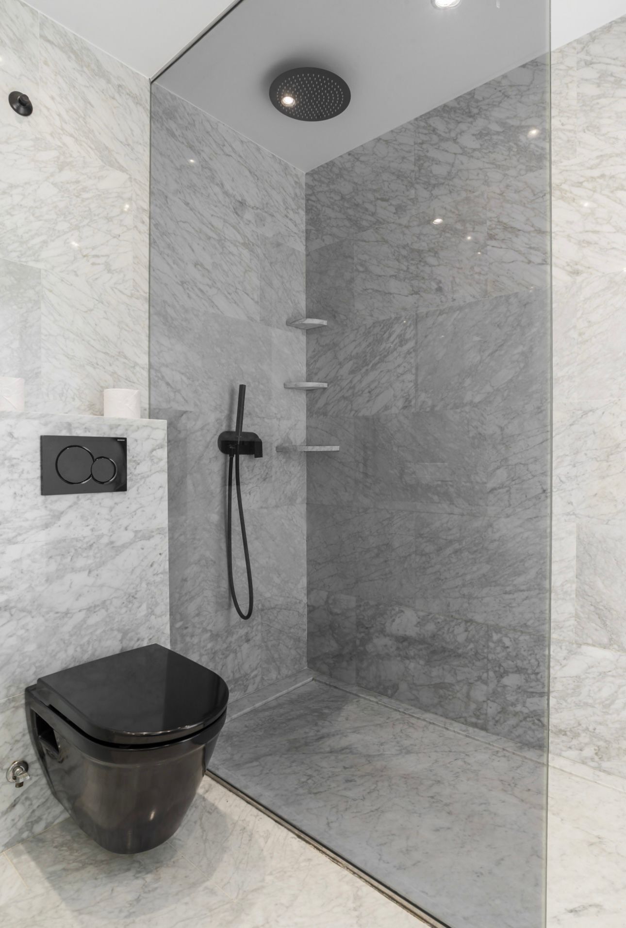 Une salle de bain moderne avec une douche à l’italienne en verre, des toilettes noires et un mur en marbre.