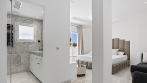 A modern bedroom with a large bed, a bedside table, and a window with curtains. - Villa Elviria (Marbella)