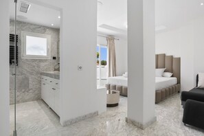 A modern bedroom with a large bed, a bedside table, and a window with curtains. - Villa Elviria (Marbella)