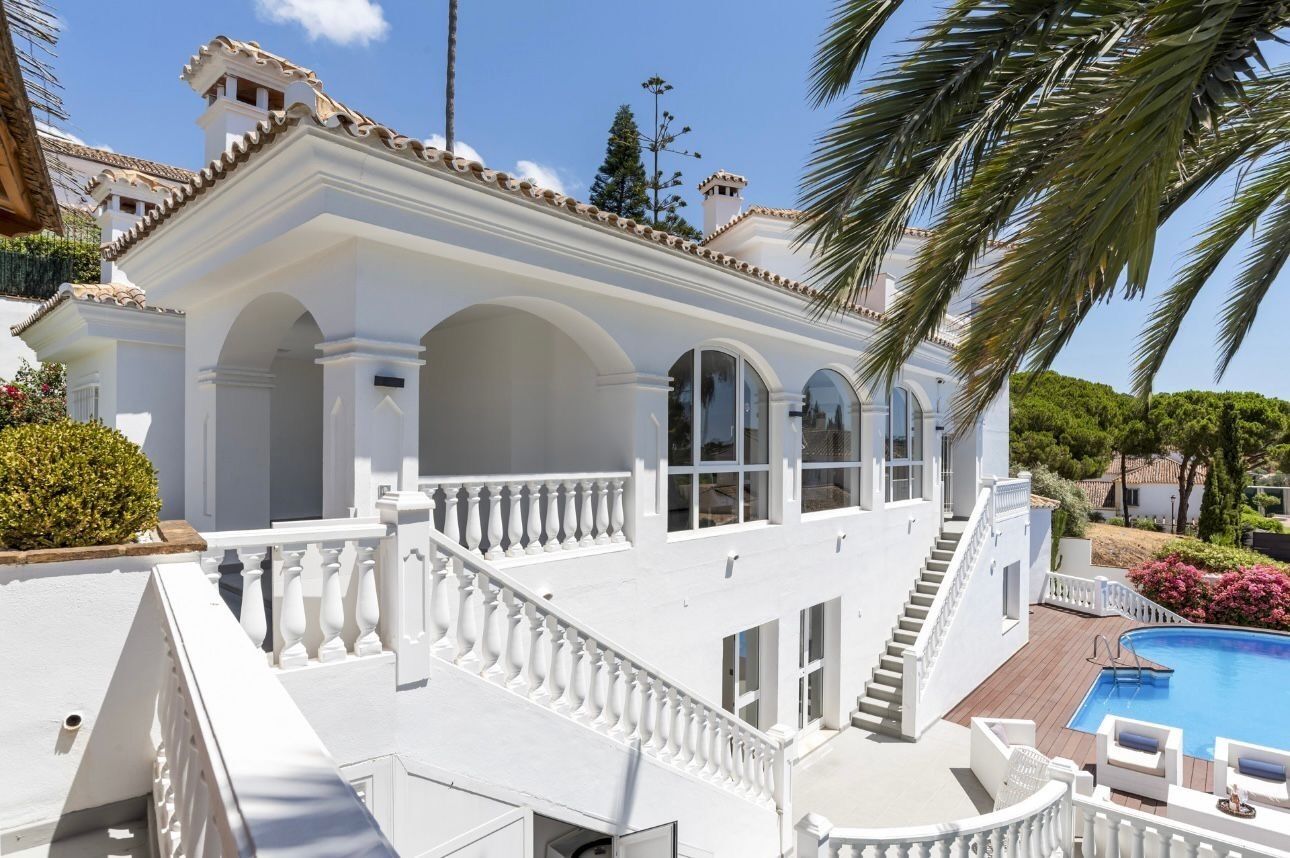 A white building with a balcony, a pool, and a staircase.