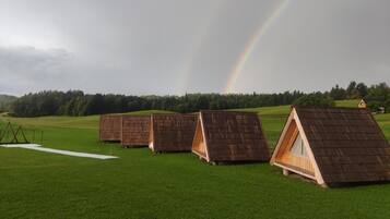 Una hilera de estructuras con techo de madera en un campo cubierto de hierba, con un arcoíris al fondo.