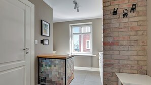 Una cocina con salpicadero de azulejos, una ventana con persianas y una pared de ladrillo con sillas fijadas a la pared.