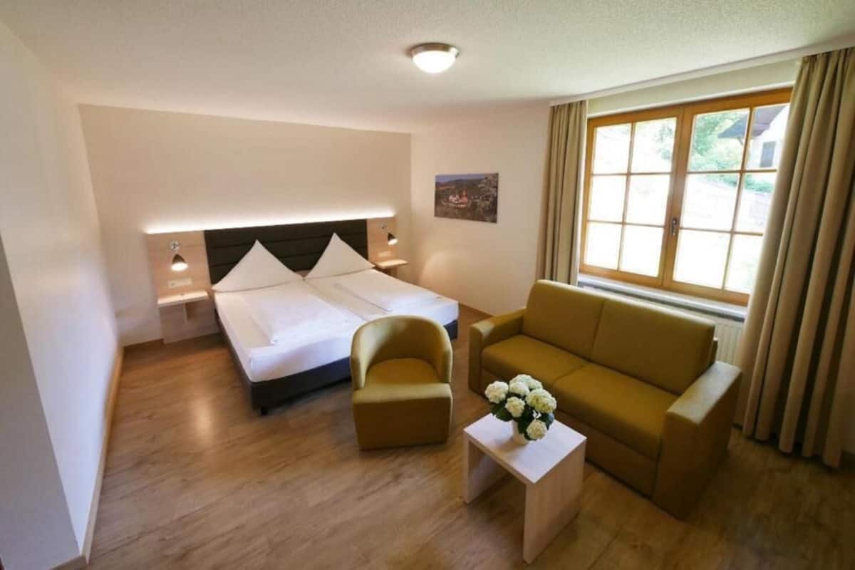 A hotel room with a bed, a sofa, a small table, and a window with curtains.
