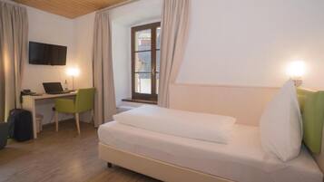 Habitación de hotel con cama, escritorio con computadora, silla, televisor montado en la pared y ventana con cortinas.