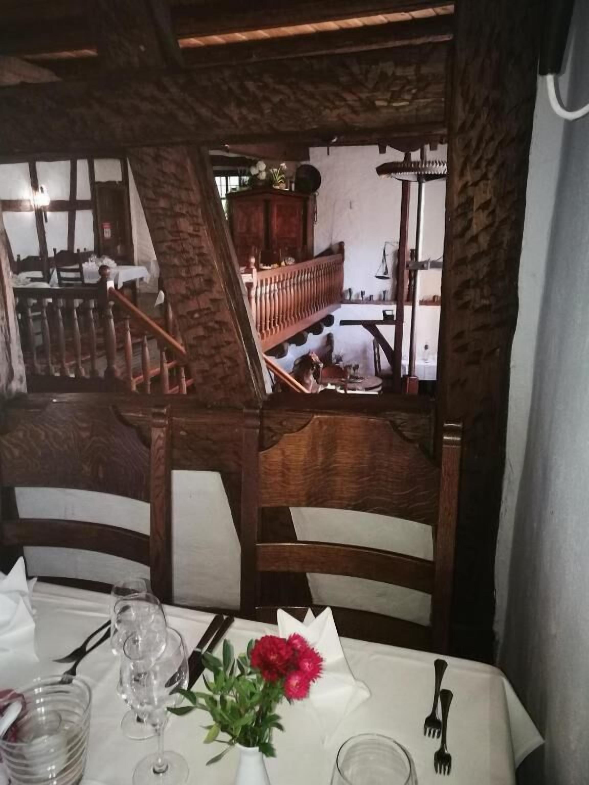 A dining table set with white tablecloth, wine glasses, a vase with red flowers, and cutlery.