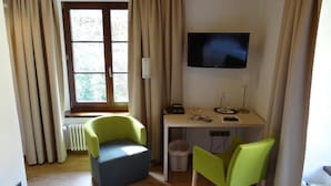 A room with a desk, two chairs, a television, and a window with curtains.