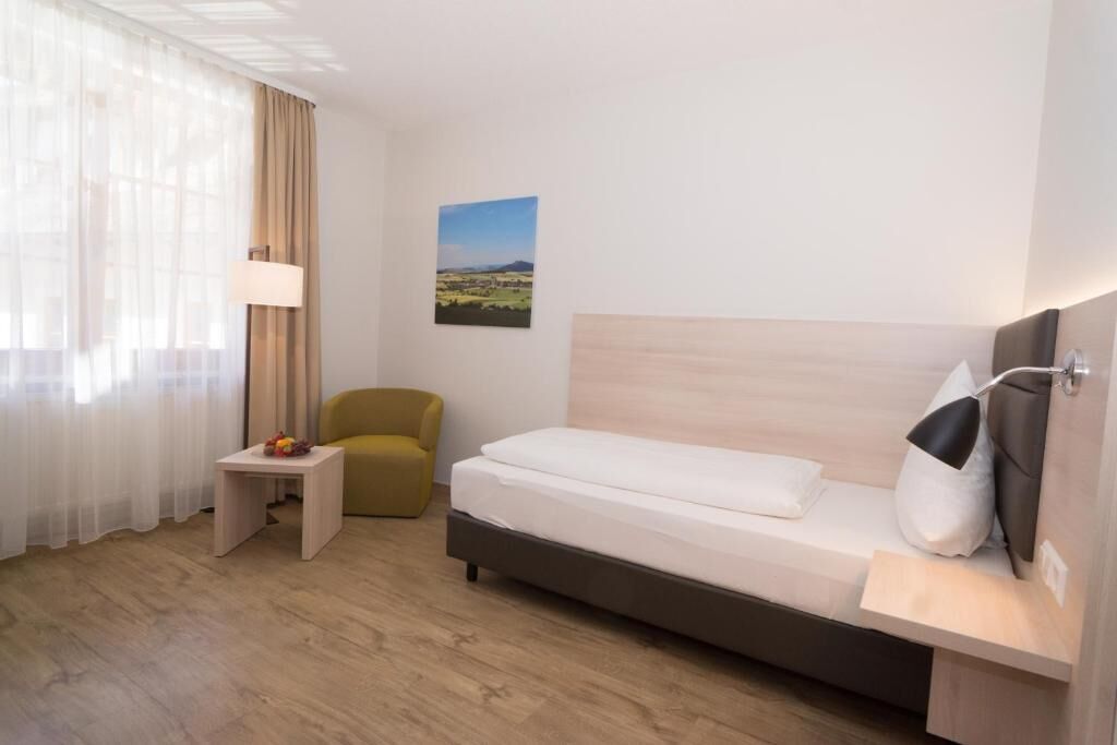 Ein Hotelzimmer mit Bett, kleinem Tisch, Stuhl, Lampe und einem Wandbild.