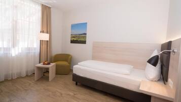 Ein Hotelzimmer mit Bett, kleinem Tisch, Stuhl, Lampe und einem Wandbild.