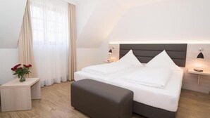 A modern hotel room with a bed, bedside tables, a nightstand, and a window with curtains.