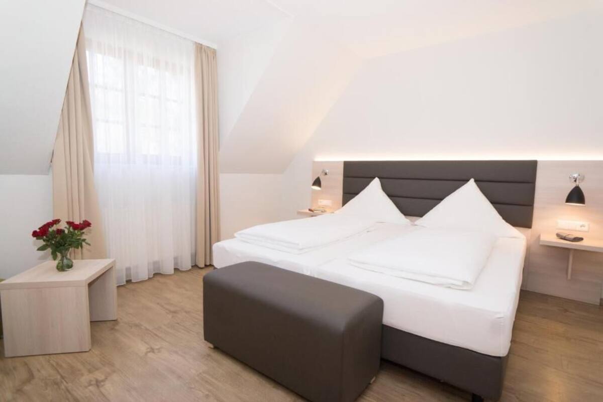 A modern hotel room with a bed, bedside tables, a nightstand, and a window with curtains.