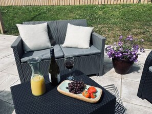 An outdoor seating area with a wicker sofa, a table with a bottle, a glass of wine, a pitcher of orange juice, and a plate of grapes and strawberries. - Tumbledown Croft.
Beautiful cottage in Aberdeenshire countryside near Cruden Bay (Hatton)