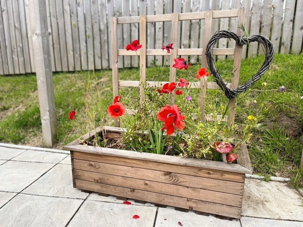 A wooden planter box with red flowers and a heart-shaped decoration.