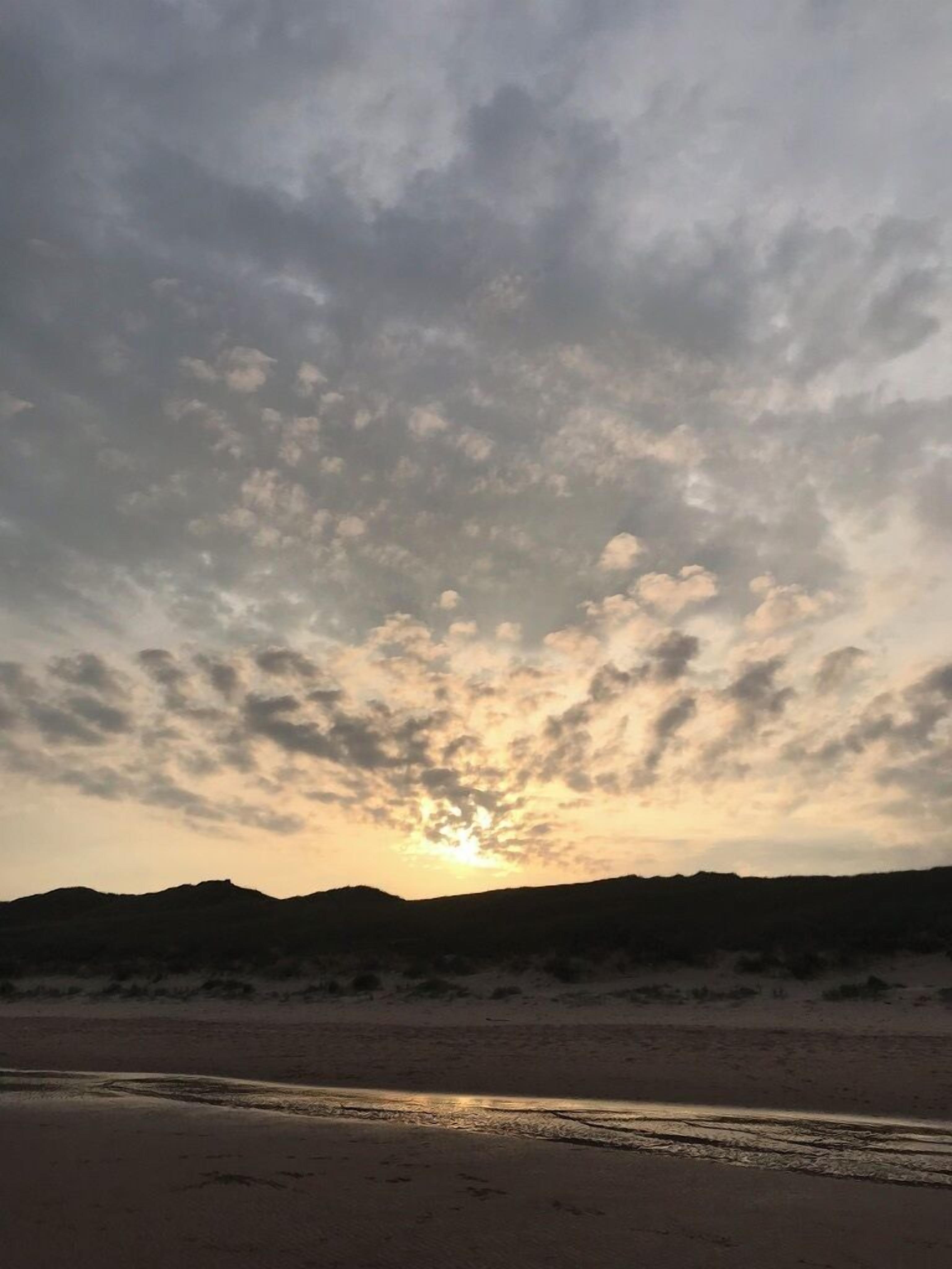 Uma praia com um pôr do sol e nuvens dispersas.