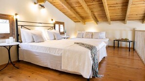 Une chambre avec un plafond en bois, deux lits, des tables de chevet et une petite table sur laquelle est posée une plante.