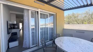 A balcony with a sliding glass door, a table with chairs, and a view of a coastal area.