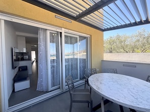 Ein Balkon mit Glastür, einem Tisch und Stühlen sowie Blick auf die Küste.