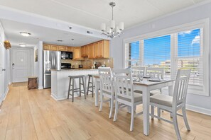 Eine moderne Küche mit Holzausstattung, einem Edelstahlkühlschrank und einer Essecke mit weißen Stühlen und einem Tisch.