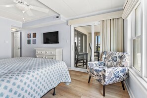 Ein Schlafzimmer mit Bett, Sessel, Fernseher und einer Glastür, die auf einen Balkon führt.