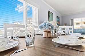 Ein Esstisch mit klarem Glas, weißen Tellern mit blauem Blumenmuster und einer blauen Blumenkomposition.