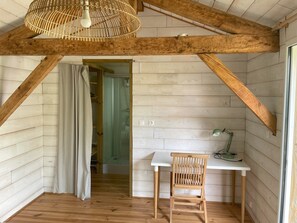 A room with wooden beams, a white desk, a chair, and a hanging light fixture.