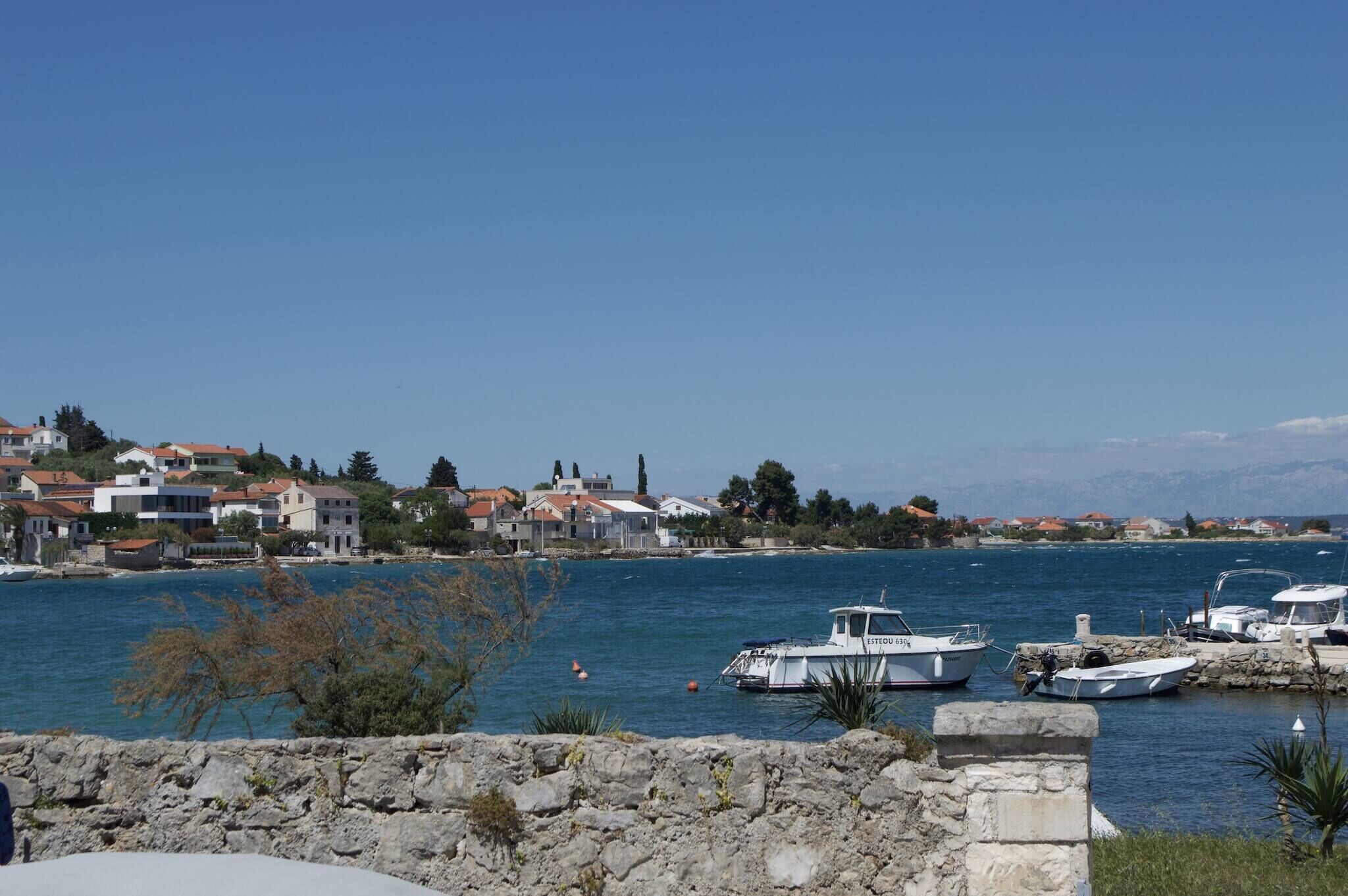 A coastal town with stone walls, boats, and buildings with red roofs.