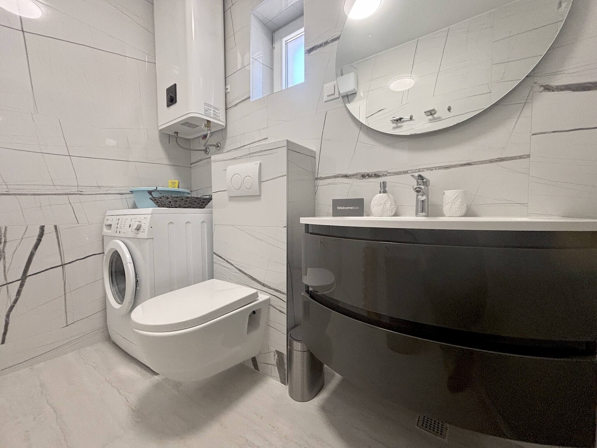 A modern bathroom with a built-in washing machine, a toilet, a sink with a mirror, and a towel rack.