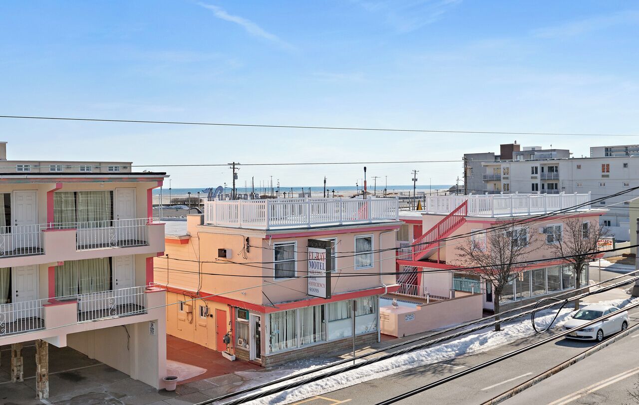 A multi-story motel with balconies, a parking lot, and a view of the beach.